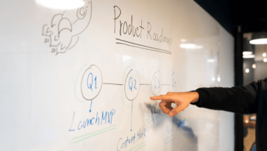 the product roadmap of a company written on a whiteboard and being discussed by an employee
